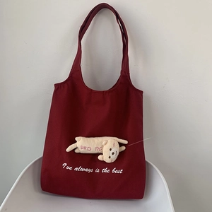 Detail of burgundy canvas tote bag with a 3D yellow bear plush and white embroidery