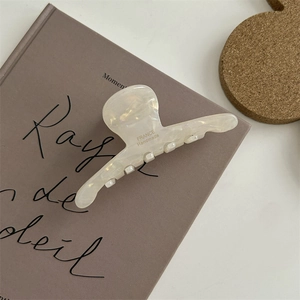 Dettaglio della pinza per capelli in acetato bianco perlato con scritta France Handmade su libro