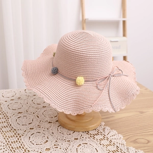 Close-up of pink straw hat with wavy brim and colorful pom-poms on wooden stand