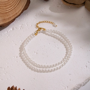 Dettaglio della collana di perle bianche a doppio strato con chiusura in oro su fondo rustico