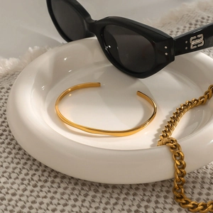 Detail of gold open bangle and chunky metal chain on a white porcelain plate