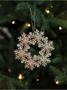 Detail of champagne gold glitter snowflake wreath ornament hanging on a Christmas tree