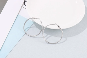 Detailaufnahme der großen silbernen Creolen mit stilvoller gestreifter Metalltextur