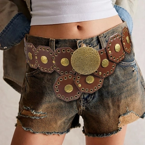 Detail of vintage wide leather belt with hollow hexagonal metal discs on denim shorts