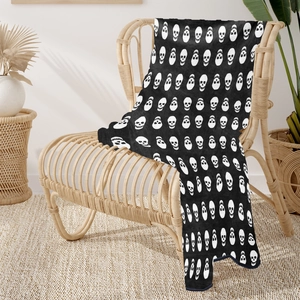 Close-up of black and white skull pattern flannel blanket draped over a rattan chair