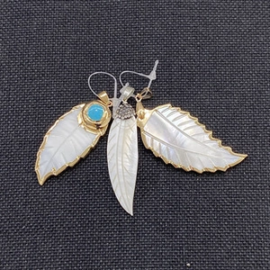 Macro detail of three leaf-shaped shell pendants with gold edges and inlaid gemstones