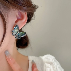 Detail of blue-green gradient butterfly stud earrings with gold foil on model
