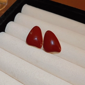 Macro shot of dark red enamel studs with gold trim in a beige velvet jewelry box