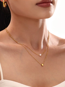 Detail of layered gold titanium steel necklace with star and pearl pendants on model