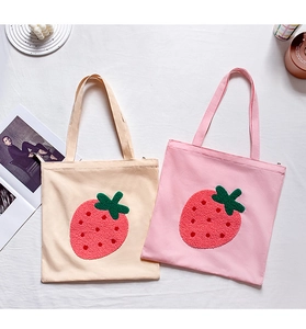 Detail of embroidered strawberry patterns on beige and pink canvas tote bags