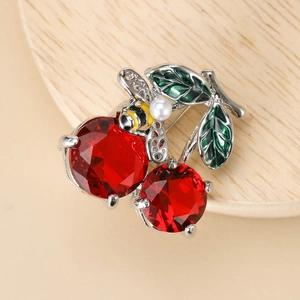 Detailed close-up of a silver cherry brooch with red crystals and a small bee on wood