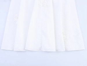 Detailed macro view of white maxi dress hem with 3D floral embroidery and jacquard texture