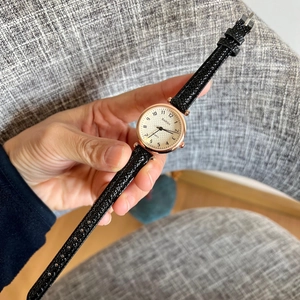 Detail view of women's gold watch with white textured dial and black leather strap