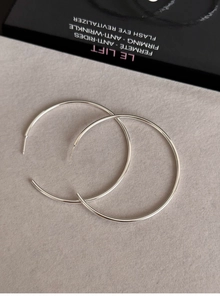 Macro shot of minimalist silver round C-shape hoop earrings on textured background