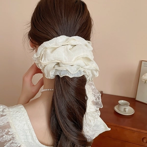 Detailed back view of a soft cream ruffled scrunchie worn on a messy bun hairstyle