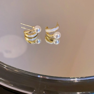 Close-up of golden C-shaped hoop earrings with white enamel and elegant pearl detail