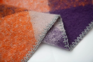 Macro shot of thick wool blend fabric with orange and purple plaid and gray stitching