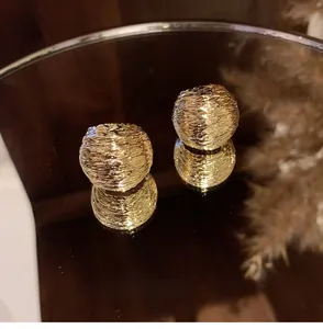 Macro shot of golden spherical stud earrings with textured finish on a mirrored tray