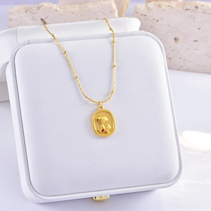 Golden rose relief necklace with small red gemstone pendant on white jewelry box