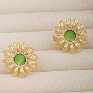 Gros plan de boucles d'oreilles marguerites dorées avec opale verte sur velours