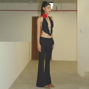 Dettaglio di un completo nero a due pezzi con fiore rosso sul top a collo alto e pantaloni