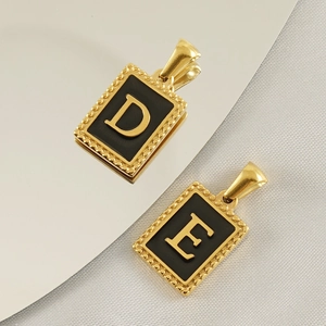 Close-up of square gold titanium steel pendants with black inlay and D and E initials