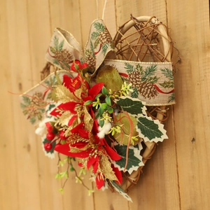 Heart-shaped Christmas wreath with red poinsettia and burlap ribbon on wood wall