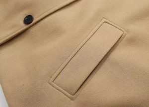 Macro detail of camel wool coat showing fabric texture, pocket seam and black button