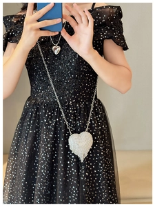 Silver heart-shaped mini rhinestone clutch bag with fine metal chain on a black dress