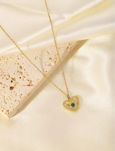 Detail of 18K gold-plated heart necklace with blue center stone on beige stone and satin