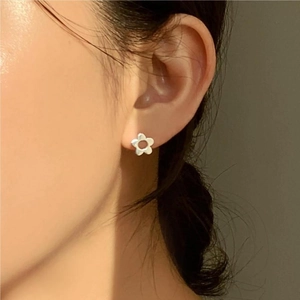 Close-up of white five-petal flower stud earring worn on ear with soft warm lighting