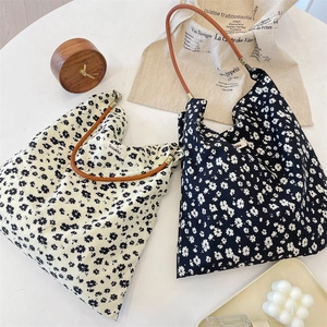 Détail du sac cabas en toile fleurie avec anses en cuir et étiquette tissée sur table