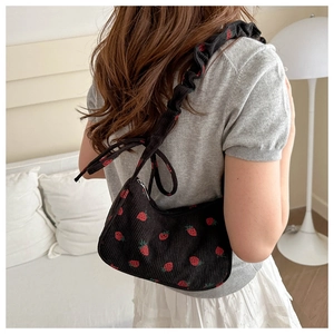 Detail of strawberry print corduroy shoulder bag with ruffled strap worn by model