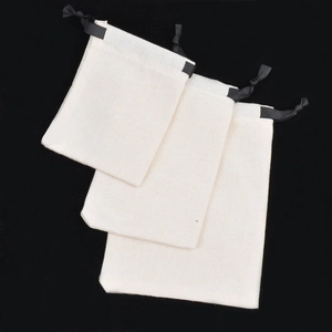 Detailed view of three sizes of cream cotton linen drawstring jewelry pouches on black