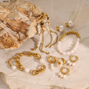 Macro shot of gold stainless steel pearl earrings and bracelet on natural stone