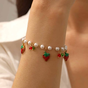 Detail of a pearl bracelet with red enamel strawberry and cherry charms on a woman's wrist