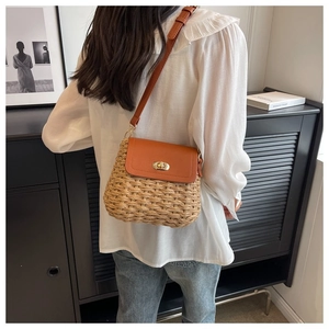 Detail of a brown woven straw crossbody bag with metal twist lock and leather adjustable strap