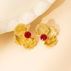 Macro detail of gold flower petal earrings with red stone and brushed texture finish