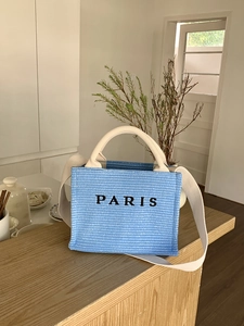 Detailed weave texture of a blue straw tote bag with white handles and Paris lettering