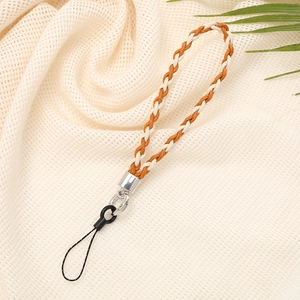 Detail of woven phone strap in orange and beige with metal clasp on natural fabric