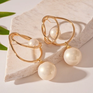 Close-up of golden geometric twisted earrings with white pearls on a stone base