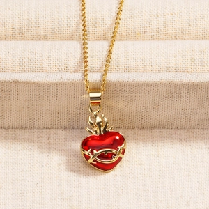 Detail of a gold heart pendant with red enamel, flame top, and thorn patterns