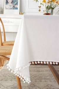 Detail of white cotton tablecloth edge featuring decorative soft pom-pom tassels