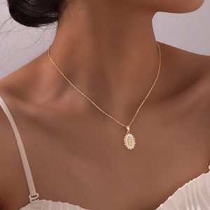Macro detail of a gold oval Virgin Mary pendant necklace with white enamel on a model