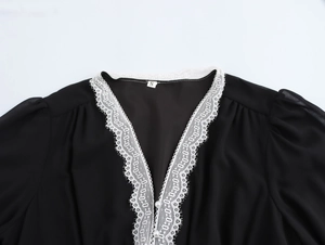 Close-up of black V-neck dress featuring delicate white lace trim and pearl buttons