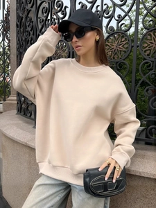 Detail of apricot crewneck sweatshirt featuring drop shoulders and ribbed cuffs in outdoor light