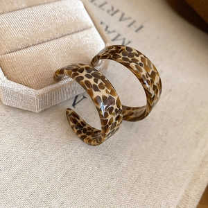 Macro view of leopard print acetate C-shape hoop earrings on a beige velvet jewelry box
