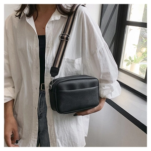 Detail of black pebble leather crossbody camera bag with stylish striped wide strap