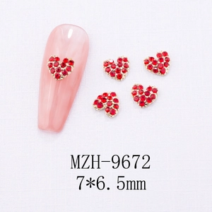 Close-up of heart-shaped nail charms with red crystals and gold base on white background