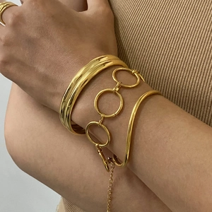 Macro view of stacked gold stainless steel bracelets and chain on model's wrist